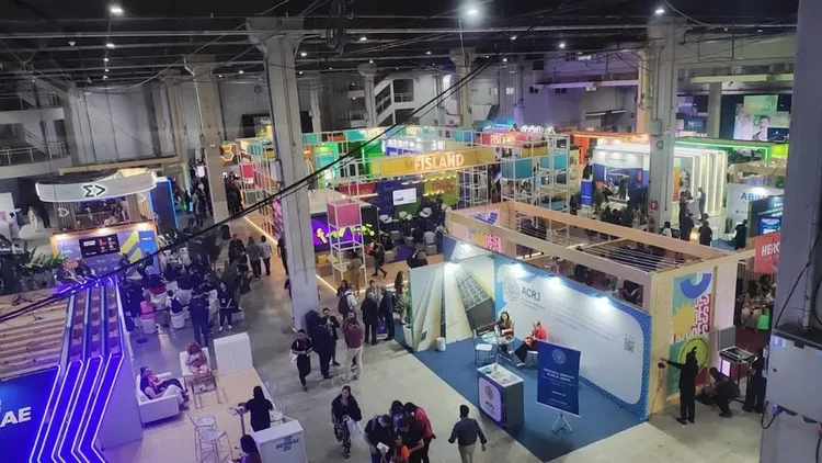 Vista do alto de pavilhão de evento com estandes e participantes