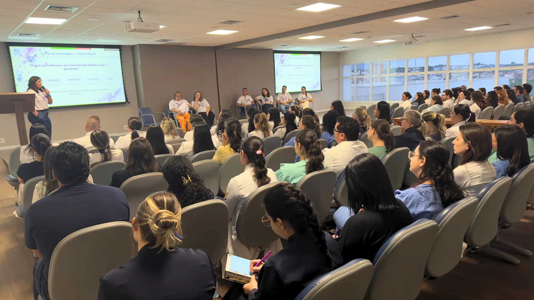 Palestrante, participantes da mesa e público em auditório durante encontro sobre cuidados paliativos