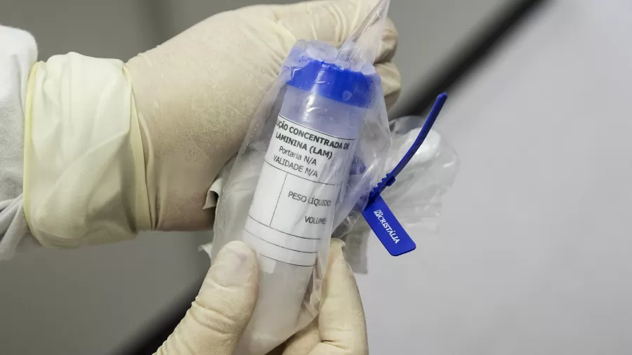 Profissional com luvas segura frasco lacrado com solução concentrada de laminina em ambiente de laboratório.