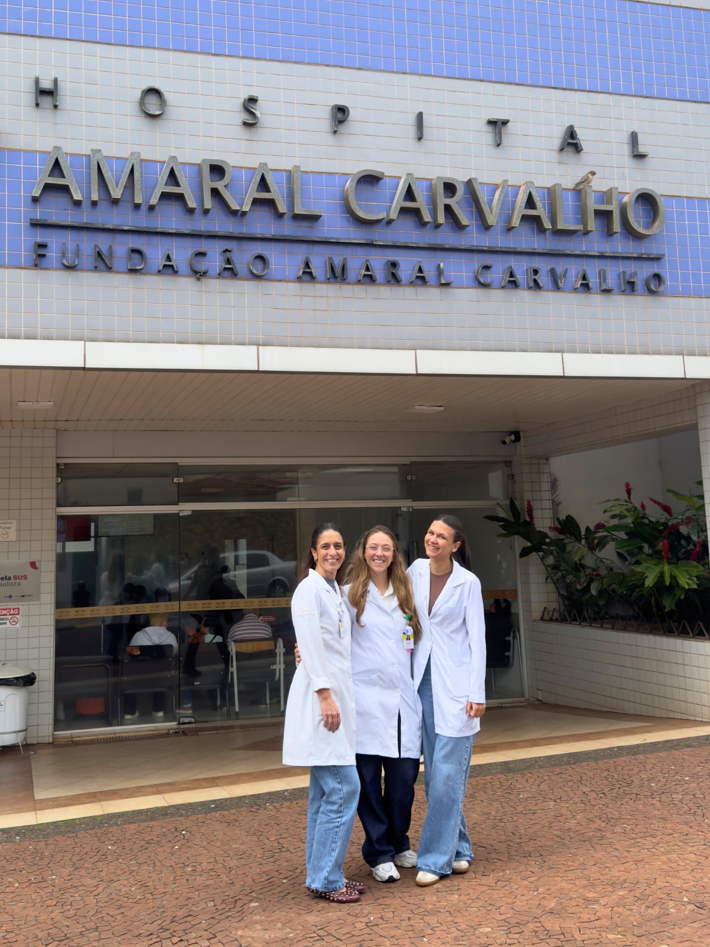 Três profissionais de jaleco em frente à fachada do Hospital Amaral Carvalho