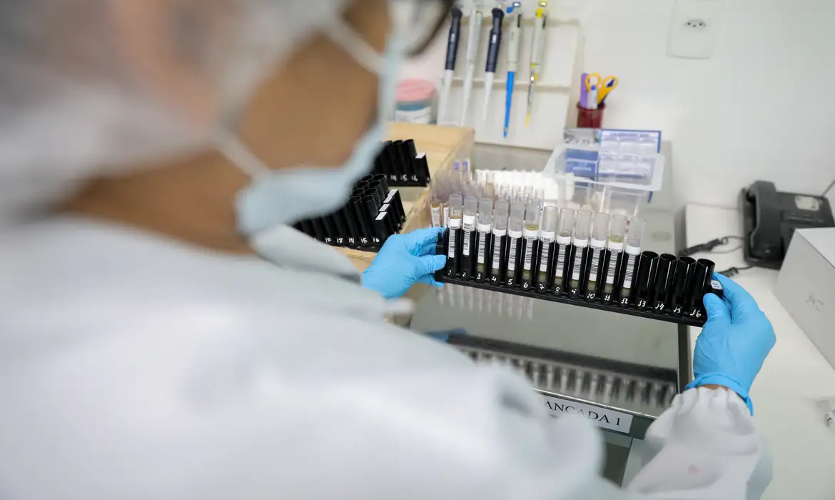 Profissional de laboratório com luvas azuis manipulando tubos de ensaio