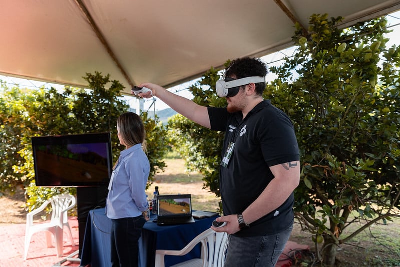 Participante usa óculos de realidade virtual em demonstração de tecnologia em área de plantação