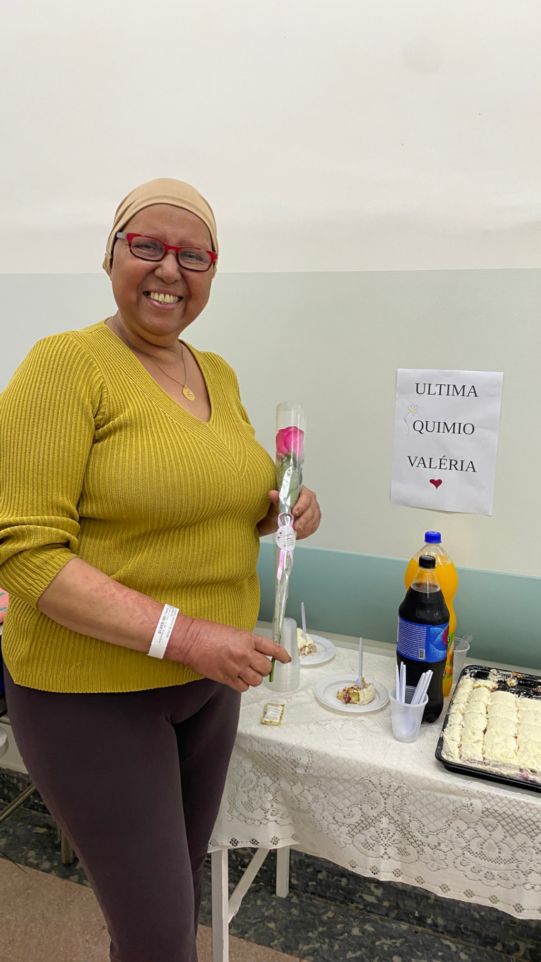 Valéria Cristina de Souza Camolesi segurando uma rosa ao lado de cartaz "Última quimio Valéria"