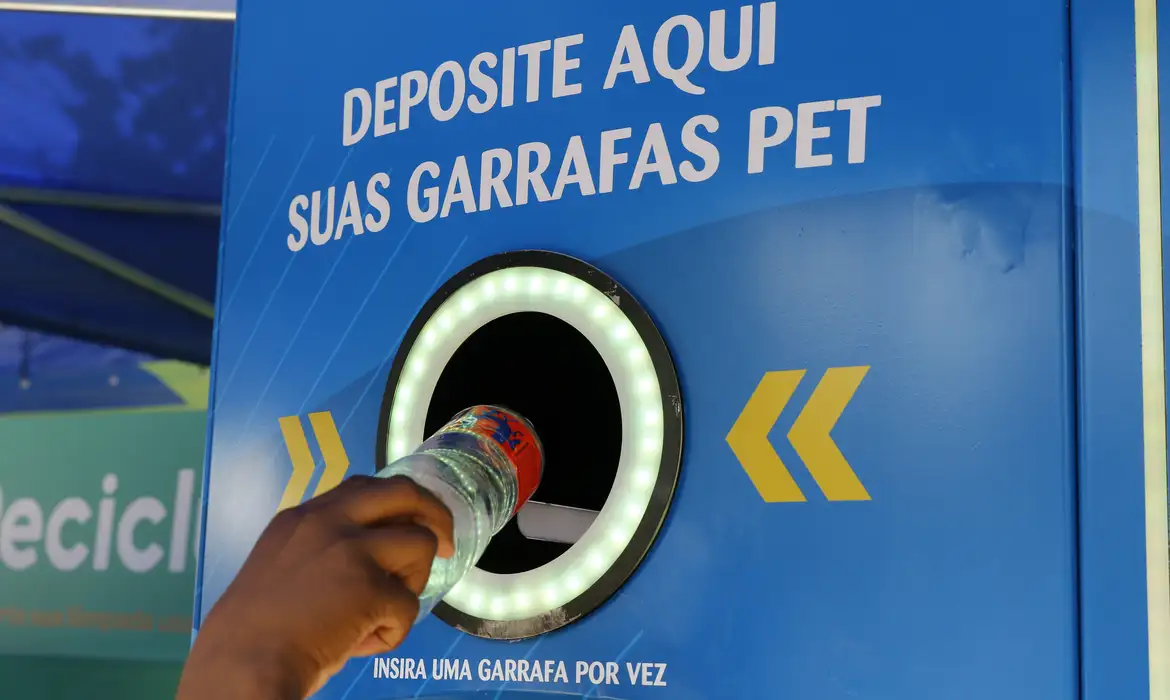 Pessoa deposita garrafa PET em máquina de reciclagem