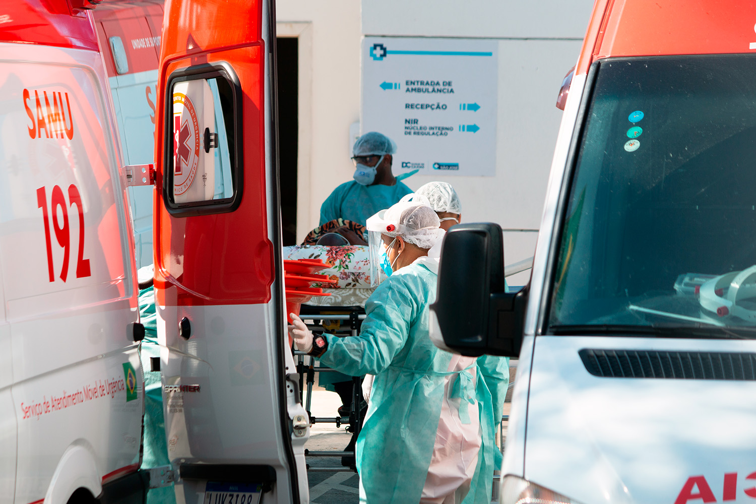 Equipe de saúde com equipamentos de proteção transfere paciente em maca entre ambulâncias do SAMU