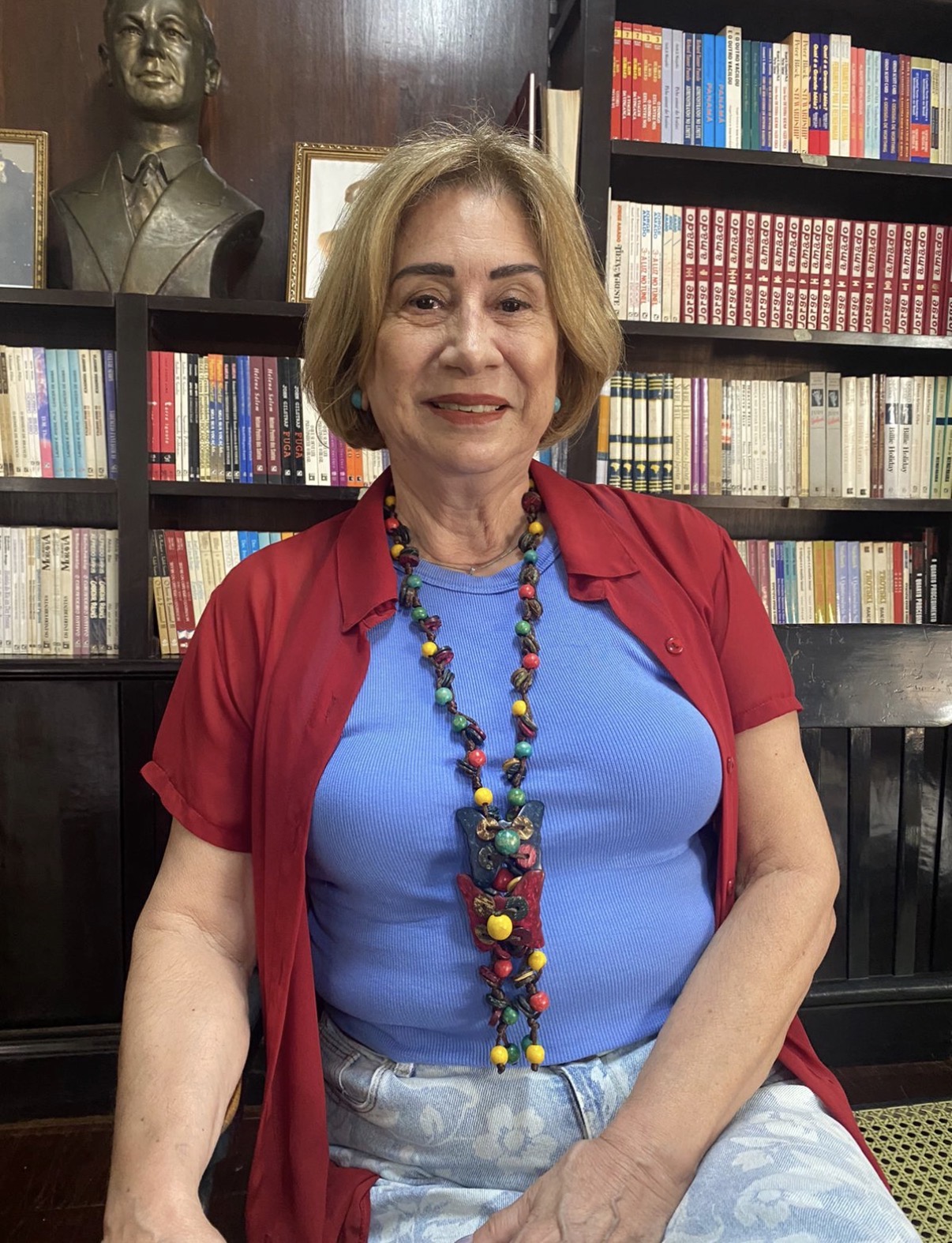 Retrato de Rachel Cesarino de Moraes Navarro sentada diante de estantes com livros